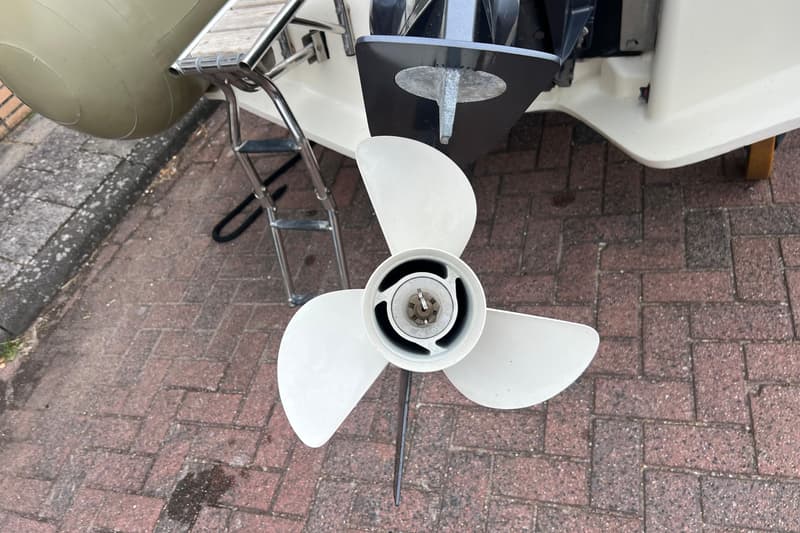 Een witte driebladige schroef van een buitenboordmotor, een zinkanode en een zwemtrap zijn zichtbaar.