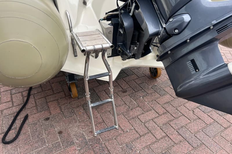 Een boot met een grijze buitenboordmotor en een opklapbare zwemtrap met houten treden, staand op een bakstenen ondergrond.