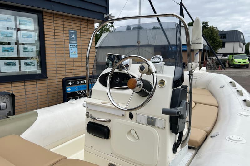 Een witte consoleboot met een stuurwiel, kompas, Yamaha-bediening en een VHF-antenne, geparkeerd bij een gebouw.