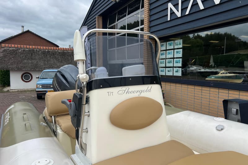 Een witte en beige boot met een Yamaha buitenboordmotor, geparkeerd voor een gebouw met de naam "Sheergold" erop.