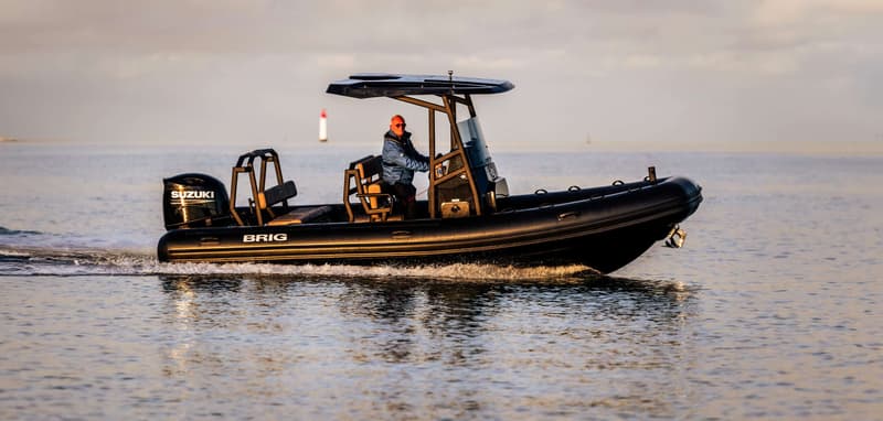 Een zwarte BRIG-boot met een Suzuki-buitenboordmotor vaart op water, met een persoon aan het roer. — BRIG Navigator
