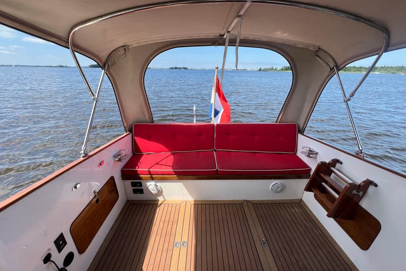 De foto toont het achterdek van een boot met een houten vloer, rode kussens en een Nederlandse vlag. — Kruiser Polyflash 950