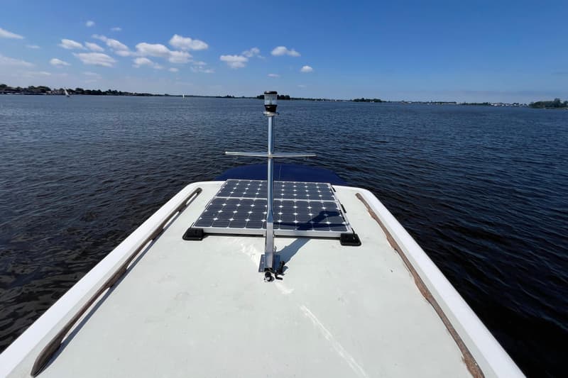 De foto toont de boeg van een boot met twee zonnepanelen en een navigatielicht, varend op een waterweg.