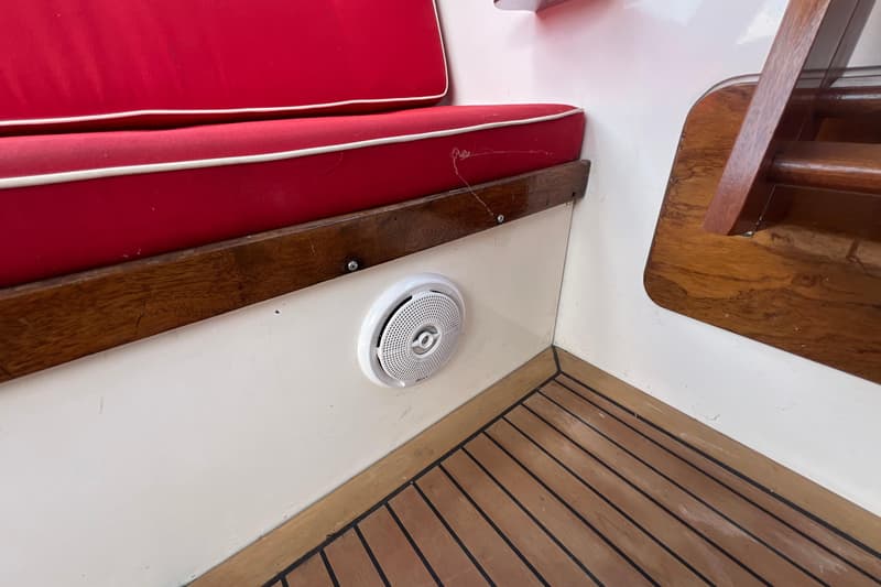 Een rode bank met witte biezen, een witte Sony-luidspreker en een houten vloer zijn zichtbaar.