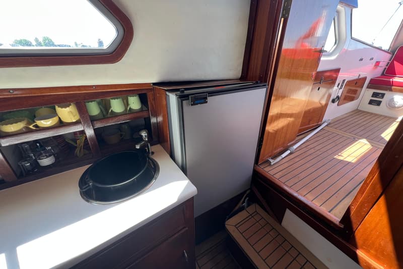 Een interieur van een boot met een gootsteen, een koelkast, een kast met servies en een houten vloer. — Kruiser Polyflash 950