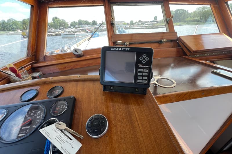 Een houten dashboard met diverse meters, een Eagle Ultra Classic dieptemeter, een afstandsbediening en sleutels.