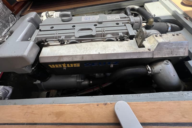 Een grijze Vetus Deutz scheepsmotor met slangen en bedrading, deels zichtbaar onder een houten vloer.