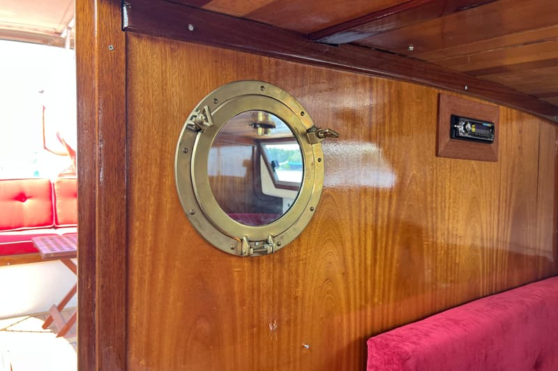 Een houten interieur met een messing patrijspoort, een ingebouwde radio en een rode bank.