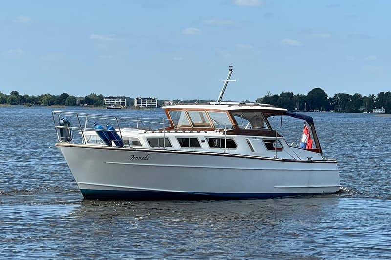 Een witte motorboot met de naam "Jenneke" vaart op een waterweg onder een blauwe lucht. — Kruiser Polyflash 950