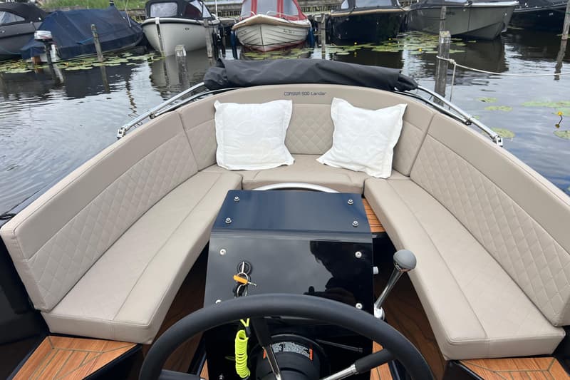 Een boot met beige gestoffeerde banken, twee witte kussens, een zwart stuur en een Corsiva 500 Tender-opschrift.