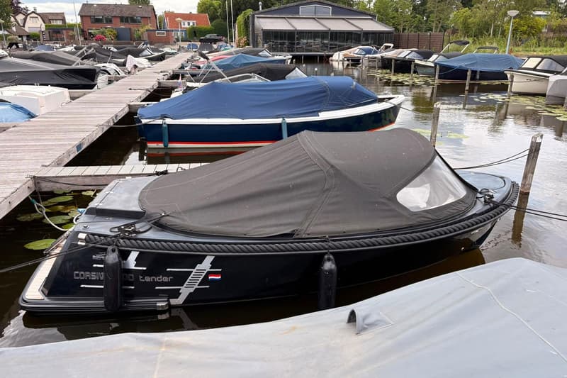 Een jachthaven met meerdere boten afgedekt met zeilen, aangemeerd aan houten steigers, met gebouwen op de achtergrond.