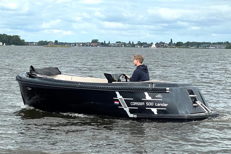 Een zwarte Corsiva 500 tender vaart op het water met een persoon aan het stuur, met op de achtergrond een dorp.