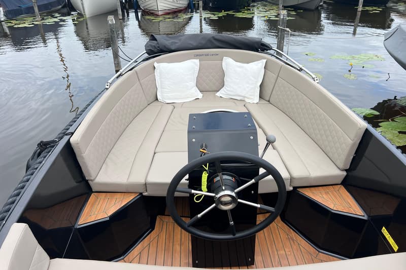 Een Corsiva 500 tender met een zwart stuur, beige kussens en twee witte sierkussens, liggend in het water.