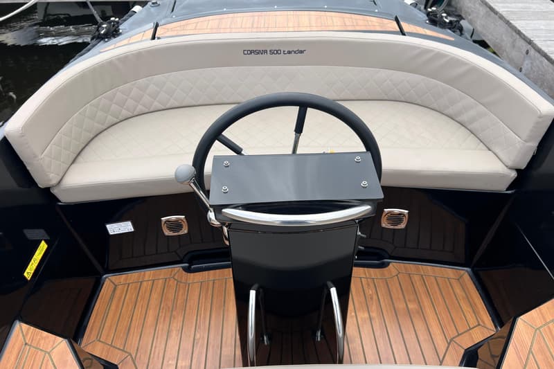 Een bovenaanzicht van het stuur en de beige gestoffeerde zitbanken van een boot met de naam "CORSIVA 500 tender".