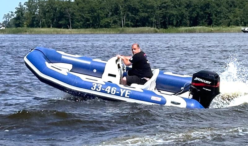 Een blauw-witte rubberboot met een man aan het stuur en een zwarte Mercury buitenboordmotor vaart over water.