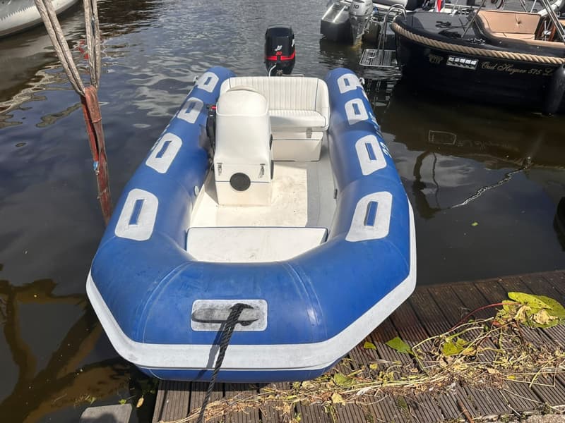 Een blauw-witte rubberboot met een buitenboordmotor ligt aangemeerd aan een houten vlonder.