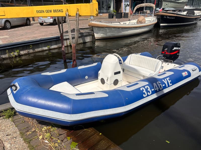 Een blauw-witte rubberboot met een buitenboordmotor en het registratienummer "33-46-YE" ligt in het water.