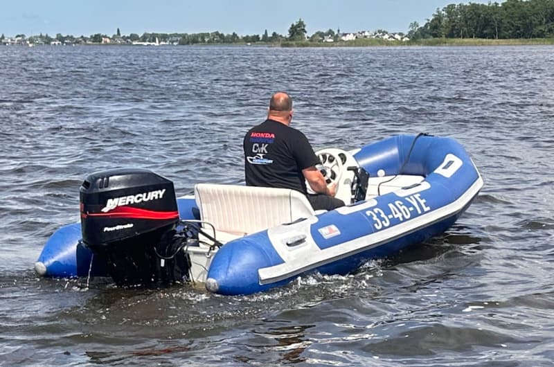 Een man in een blauw-witte rubberboot met een Mercury buitenboordmotor vaart op een meer.