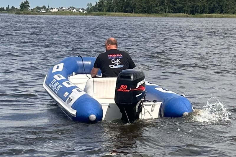 Een man in een blauw-witte rubberboot met een Mercury 50 pk buitenboordmotor vaart op het water.