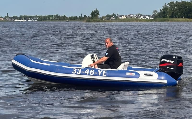 Een man zit in een blauw-witte rubberboot met een Mercury buitenboordmotor op het water.