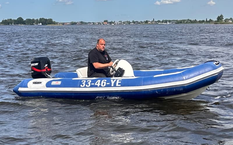 Een man zit in een blauw-witte rubberboot met een Mercury buitenboordmotor op het water.