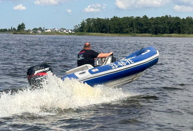 Een man in een blauwe rubberboot met witte accenten en een Mercury buitenboordmotor vaart over het water.