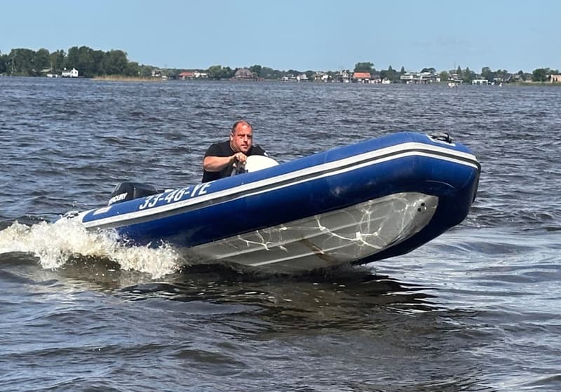 Een man vaart in een blauwe rubberboot met een buitenboordmotor over water, met een kenteken 33-46-YE.