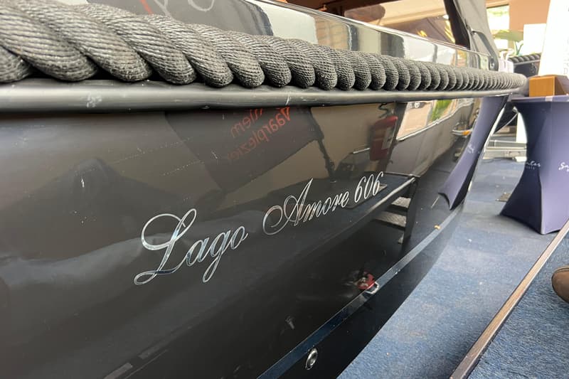 De zijkant van een donkere boot met de naam "Lago Amore 606" in zilveren letters en een dikke, gevlochten stootrand.