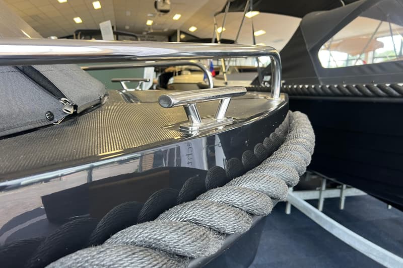 Een detailfoto van de boeg van een donkere boot met een zilveren kikker en een dikke, grijze stootrand.