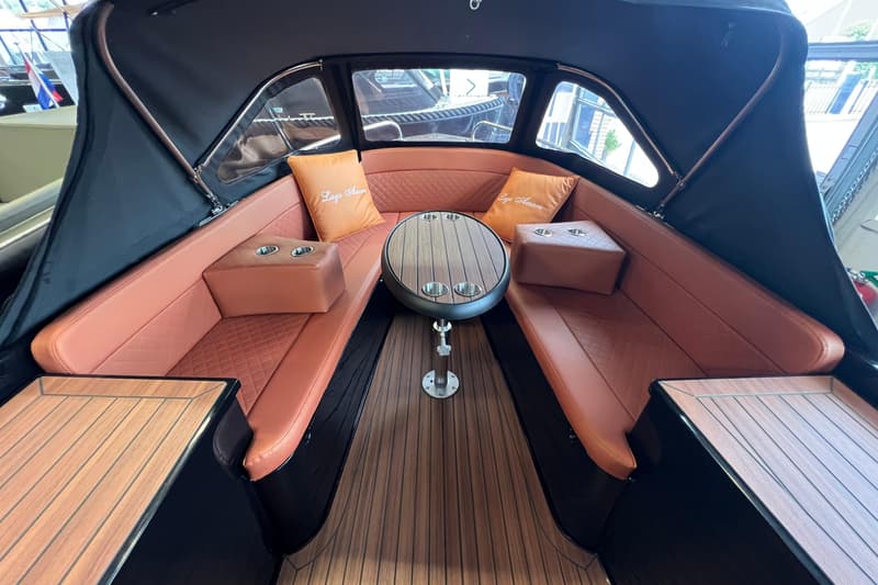 De foto toont het interieur van een boot met bruine zitbanken, een houten vloer en een tafel met bekerhouders.