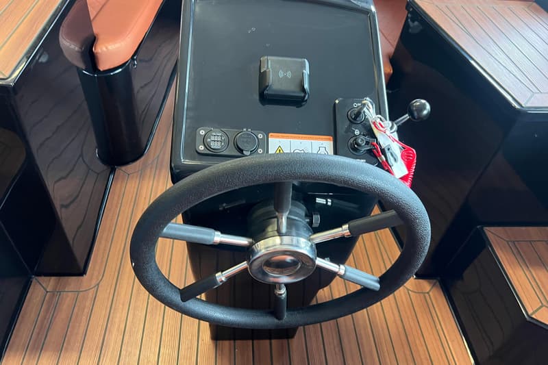 Een stuurwiel met een zwart dashboard, waarop een draadloze oplader, een voltmeter, een USB-poort en contactsleutels…