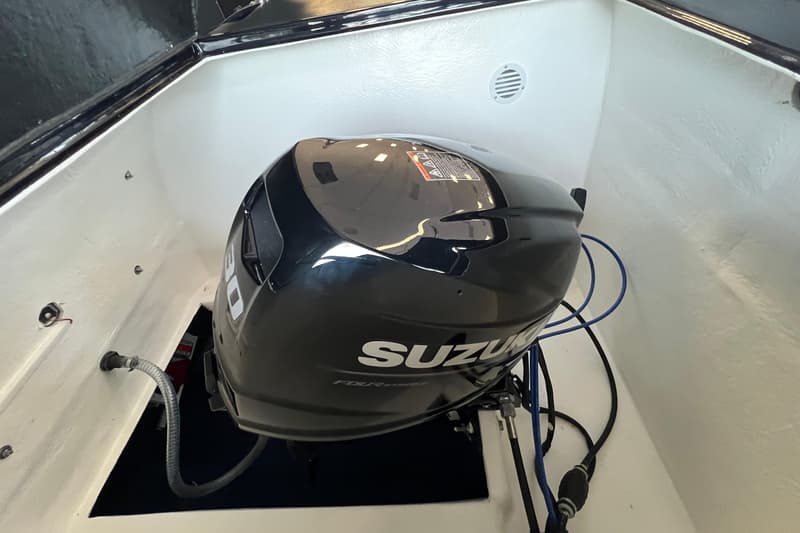 Een zwarte Suzuki buitenboordmotor met "FOUR STROKE" erop, omringd door witte bootwanden en diverse kabels.