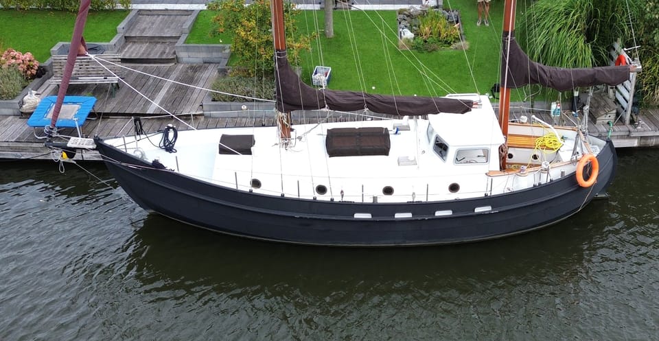 Een donkergrijze zeilboot met een witte opbouw en dek ligt afgemeerd aan een houten steiger. — Danish Rose 31
